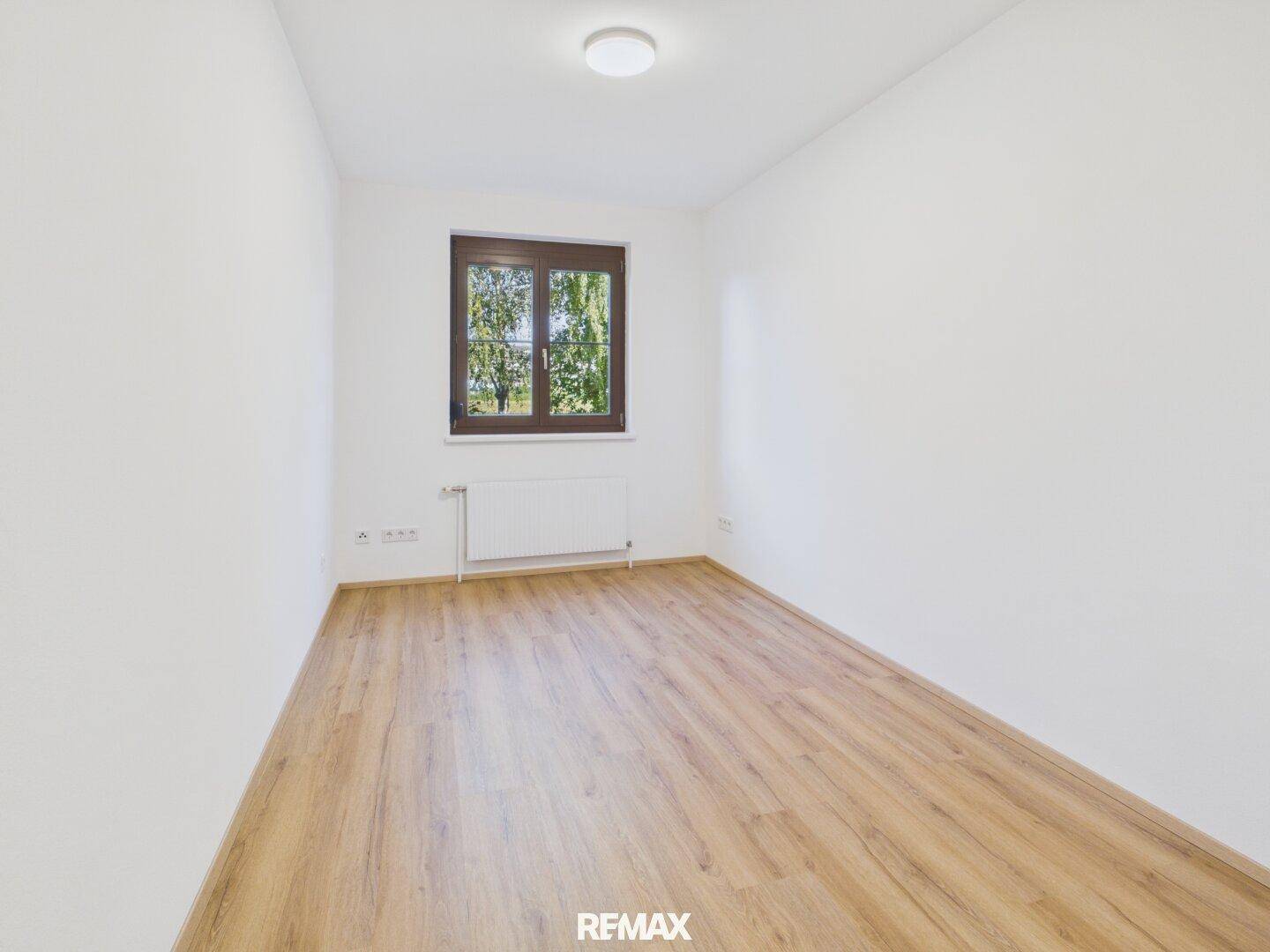 Helles Zimmer mit Laminatboden und einem Fenster, das viel Tageslicht in den Raum bringt.