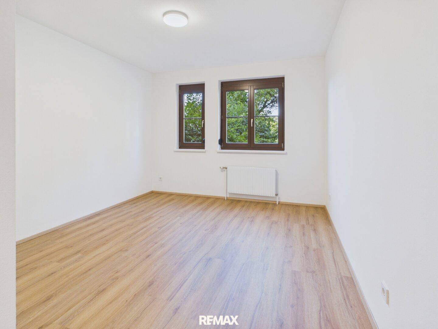 Helles Schlafzimmer mit Laminatboden, weißen Wänden und zwei Fenstern für viel Tageslicht.