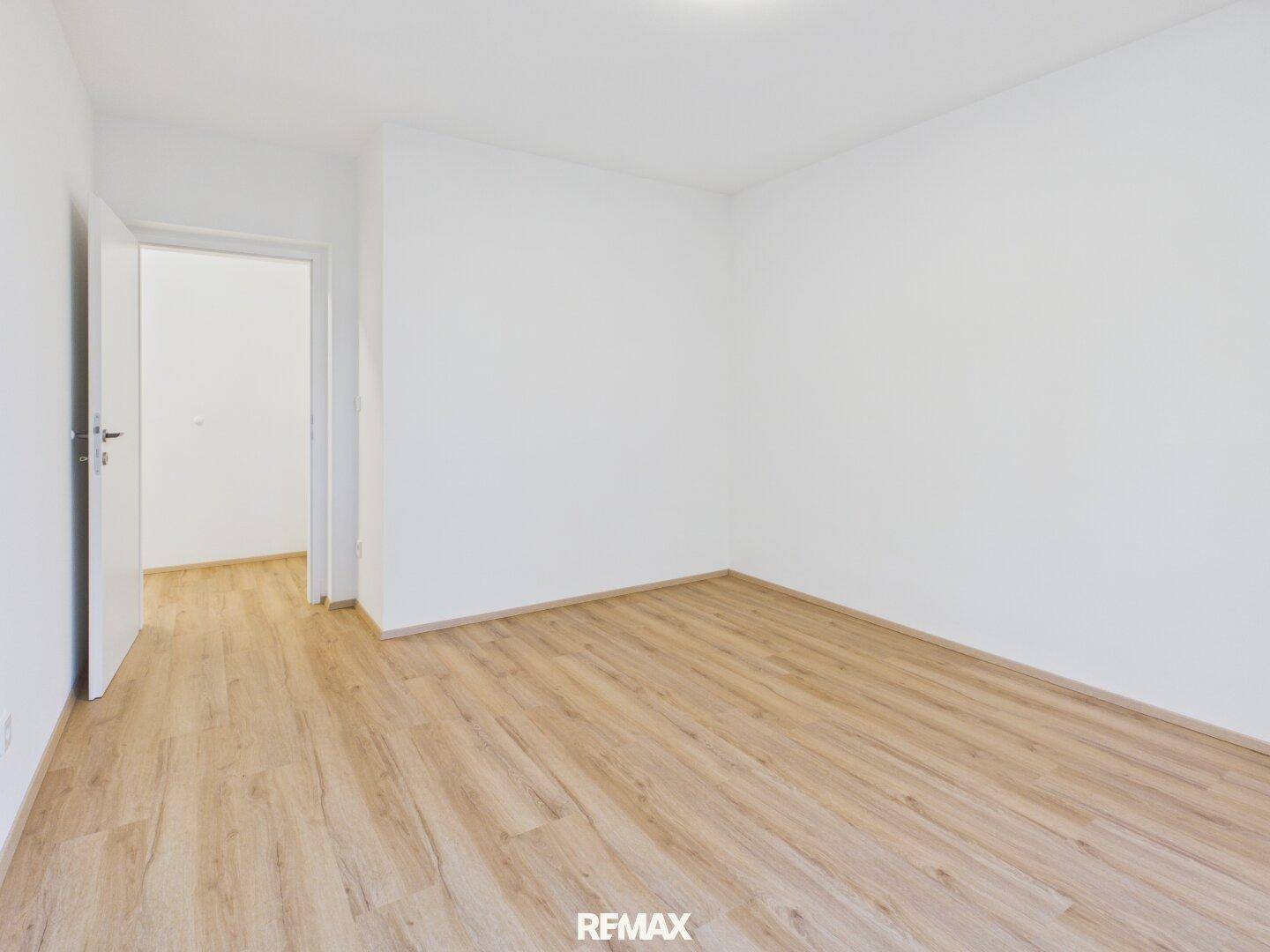 Leeres Schlafzimmer mit Laminatboden und weiß gestrichenen Wänden, bereit zum Einrichten.