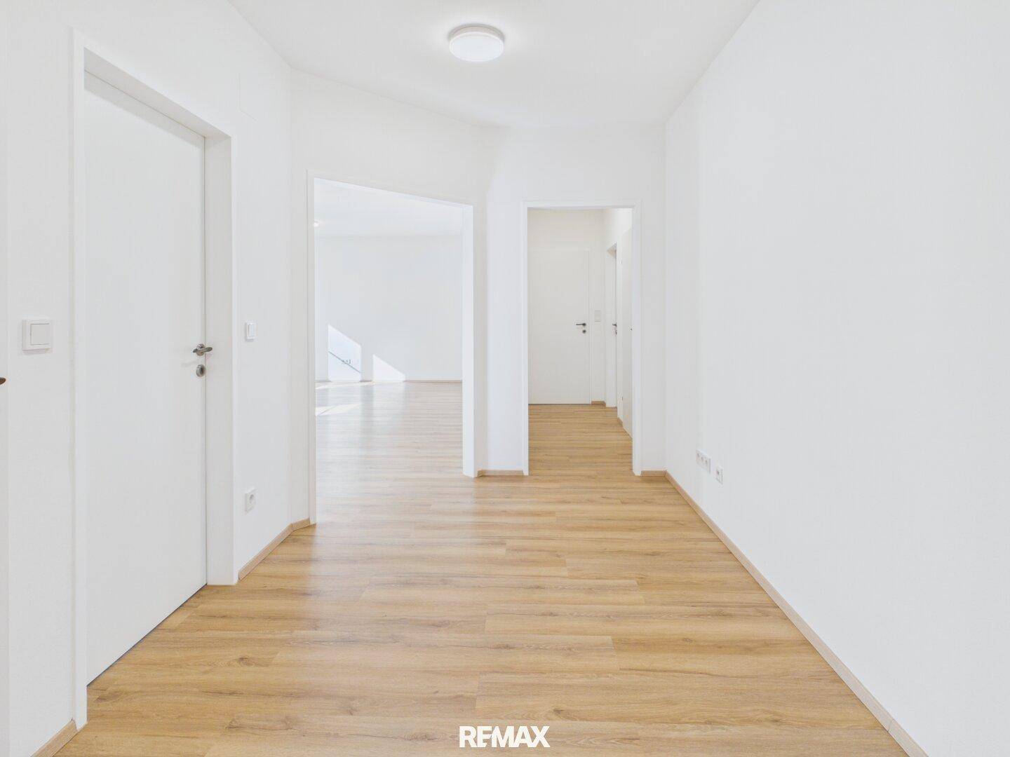 Heller Flur mit modernem Laminatboden und weißen Wänden, der zu weiteren Räumen führt.