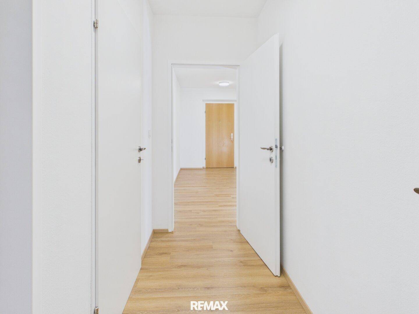 Langer, heller Flur mit Laminatboden und weißen Türen, der verschiedene Bereiche verbindet.