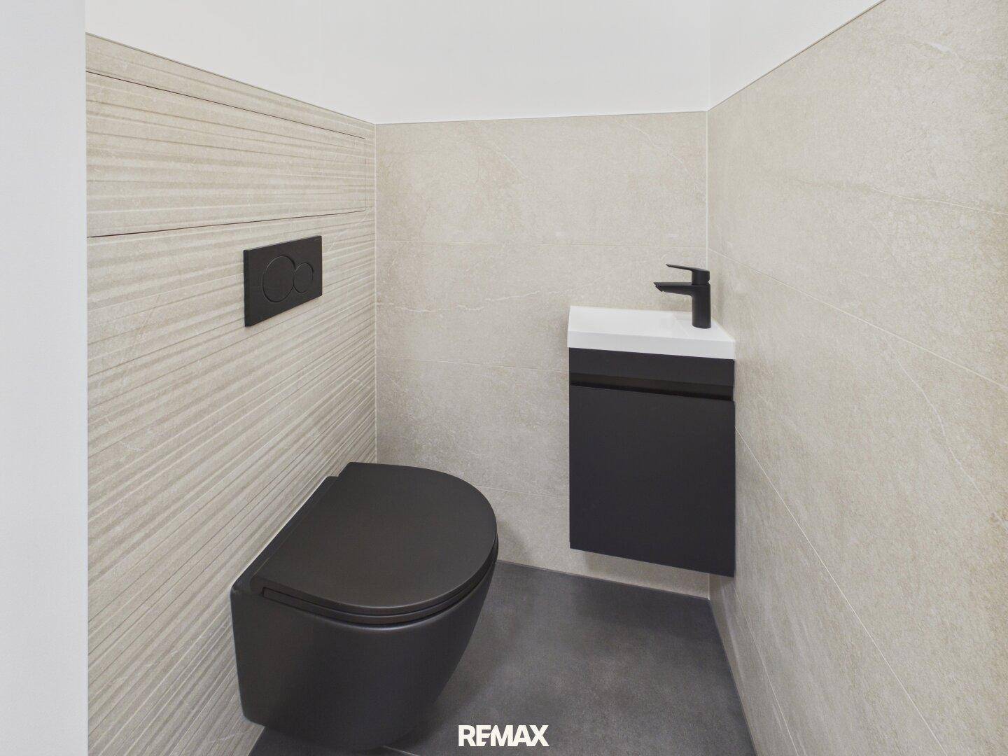 Modernes Gäste-WC mit wandhängender schwarzer Toilette und kleinem Waschbecken.