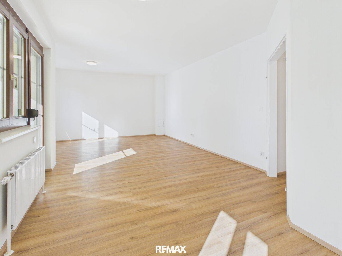 Geräumiges, helles Zimmer mit Laminatboden und großen Fenstern, ideal als Wohnbereich.
