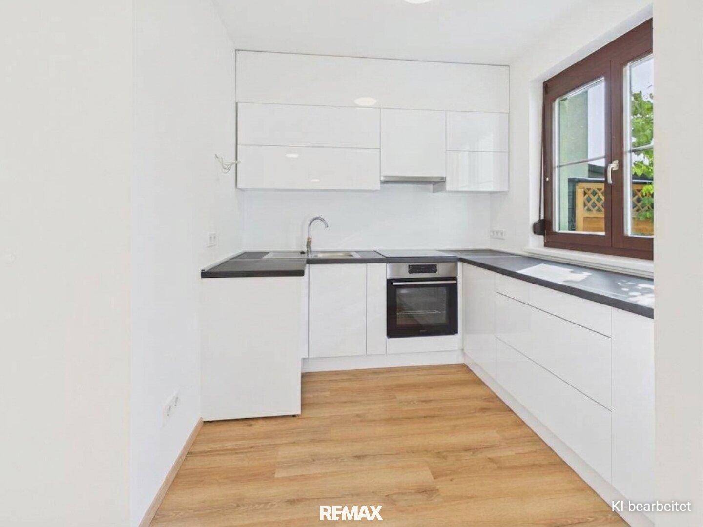 Moderne Einbauküche mit weißen Hochglanzfronten, dunkler Arbeitsplatte und Fenster.