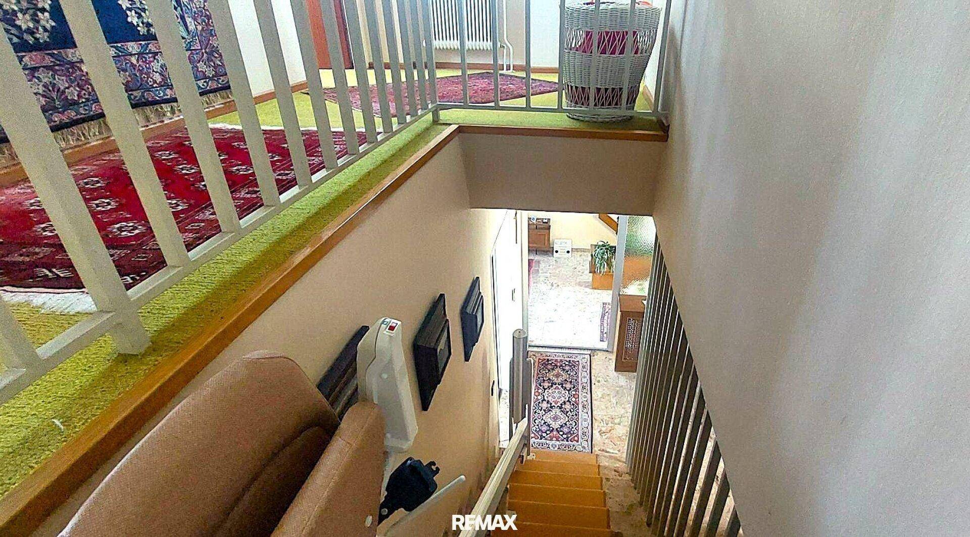 Treppenhaus mit Teppichboden und einem installierten Treppenlift für barrierefreien Zugang zu den Etagen.