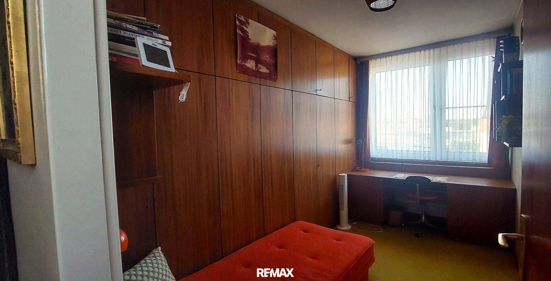 Schlafzimmer mit Holzvertäfelung, integriertem Schreibtisch und einem Fenster mit Jalousien.