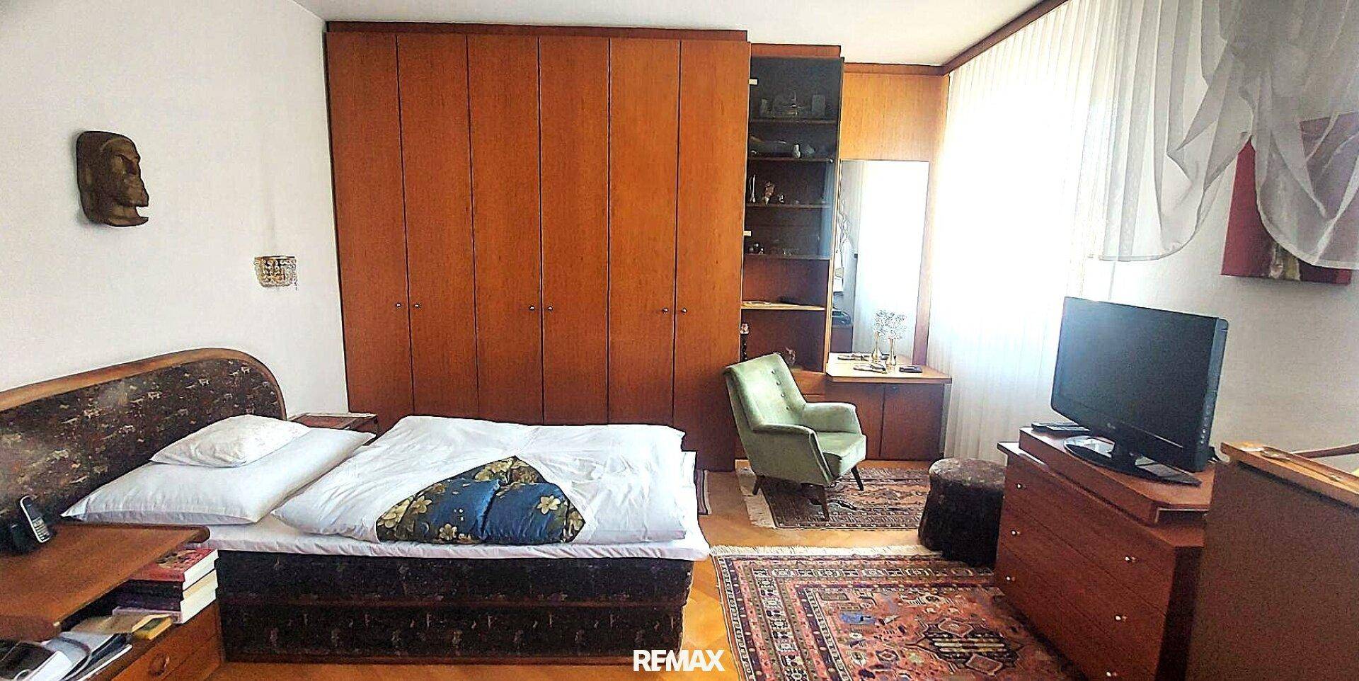 Schlafzimmer mit Doppelbett, großen Einbauschränken aus Holz und einem gemusterten Teppichboden.