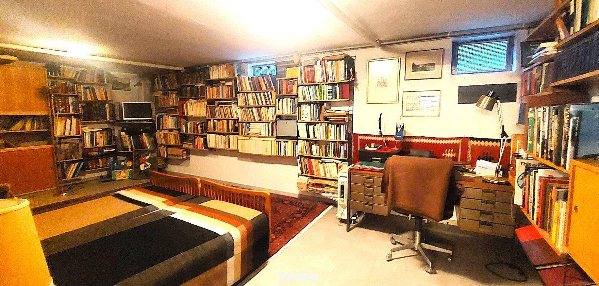 Kellerraum als Büro oder Schlafzimmer genutzt, mit vielen Bücherregalen und einem Schreibtisch.