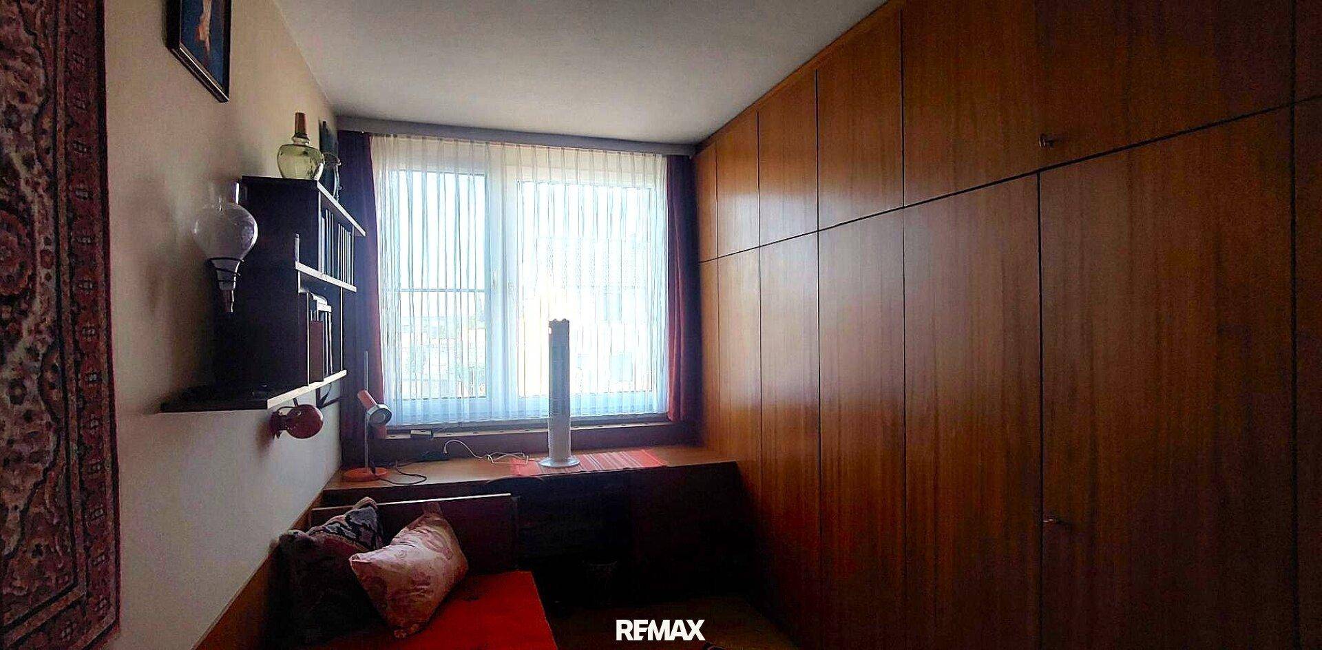 Schlafzimmer mit Holzvertäfelung, integriertem Schreibtisch und einem Fenster mit Jalousien.