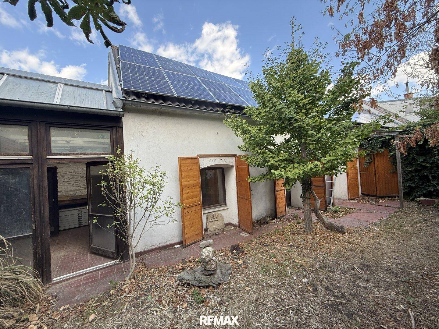 Hinterhof mit Solaranlage auf dem Dach, Bäumen und einem kleinen Gartenbereich.