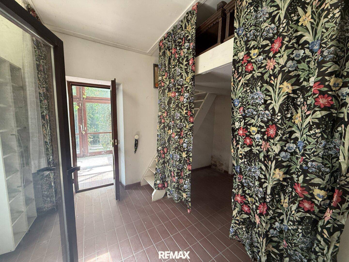 Schlafzimmer mit floralen Vorhängen, Fliesenboden und einer erhöhten Schlafebene.