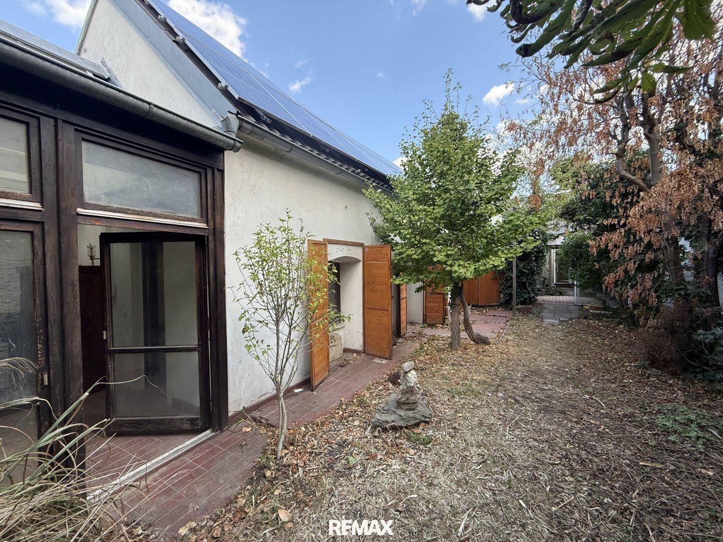 Hinterhof mit Solaranlage auf dem Dach, Bäumen und einem kleinen Gartenbereich.