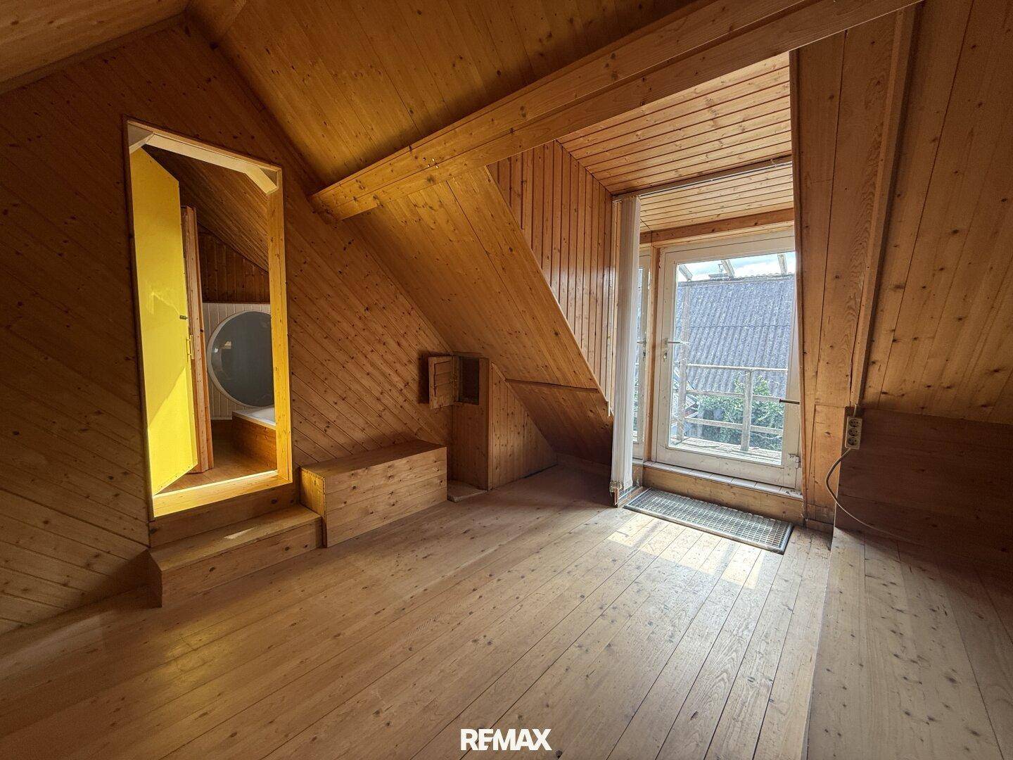Gemütliches Dachzimmer mit Holzverkleidung, Holzboden und Zugang zu einem kleinen Balkon.