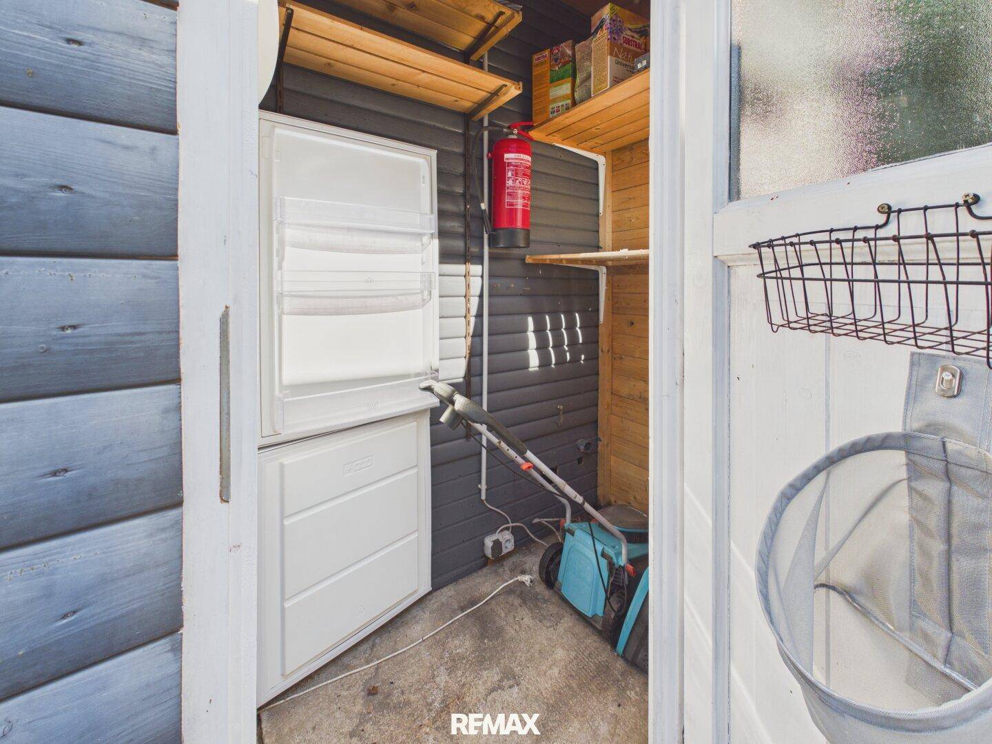 Praktischer Abstellraum mit Gefrierschrank, Regalen und Werkzeugen für den Garten.