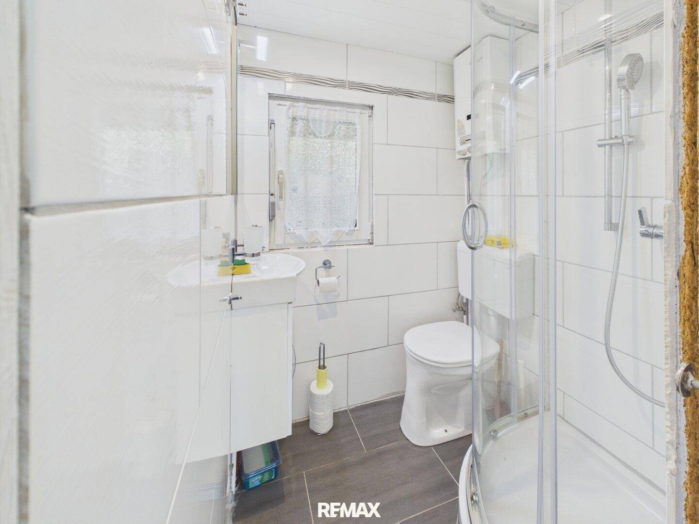 Kleines Badezimmer mit Dusche, WC, Waschbecken und weiß gefliesten Wänden.