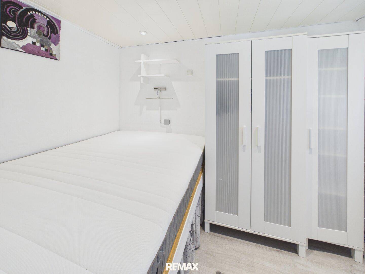 Schlafzimmer mit Einzelbett und weißem Kleiderschrank, hell und funktional eingerichtet.