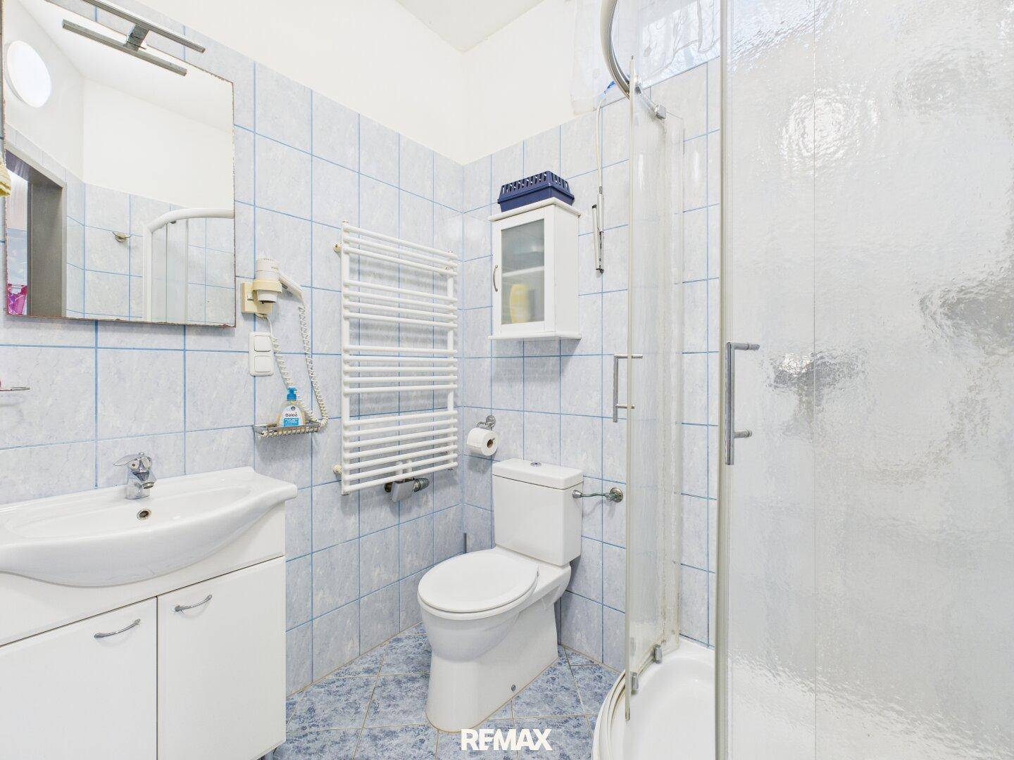 Badezimmer mit Dusche, WC, Waschbecken und hellblauen Fliesen, funktional und sauber.
