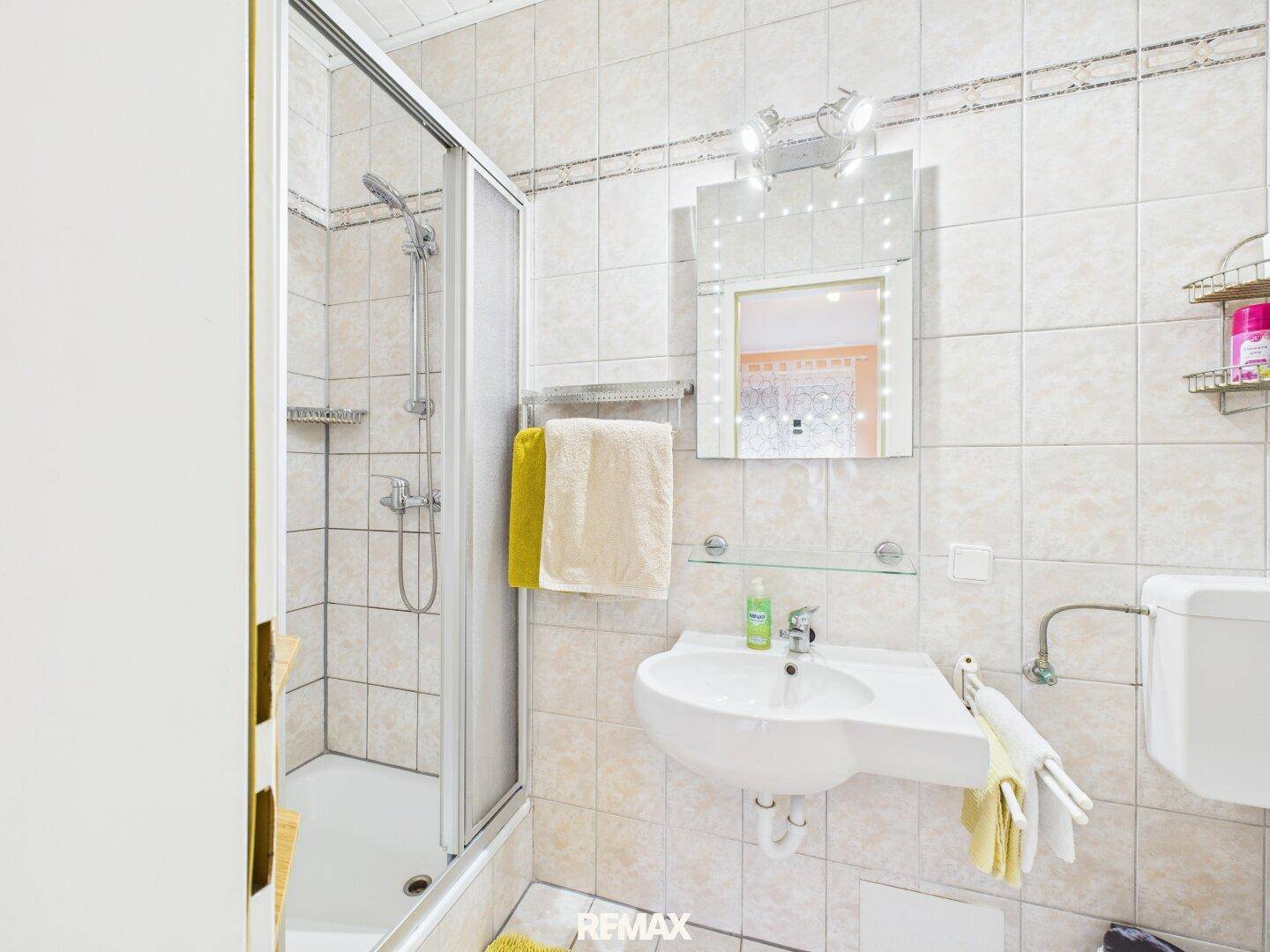 Badezimmer mit Dusche, Waschbecken und hellen Fliesen, funktional und gut gepflegt.