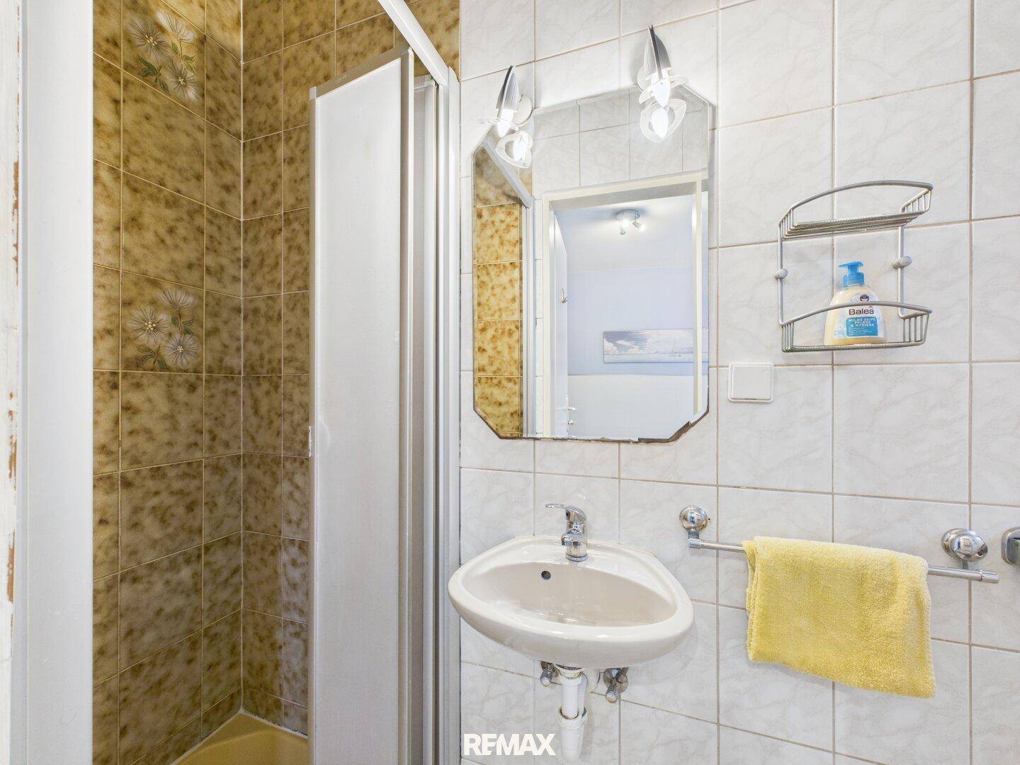 Badezimmer mit Dusche, Waschbecken und gemusterten Fliesen, im Stil der 80er Jahre.
