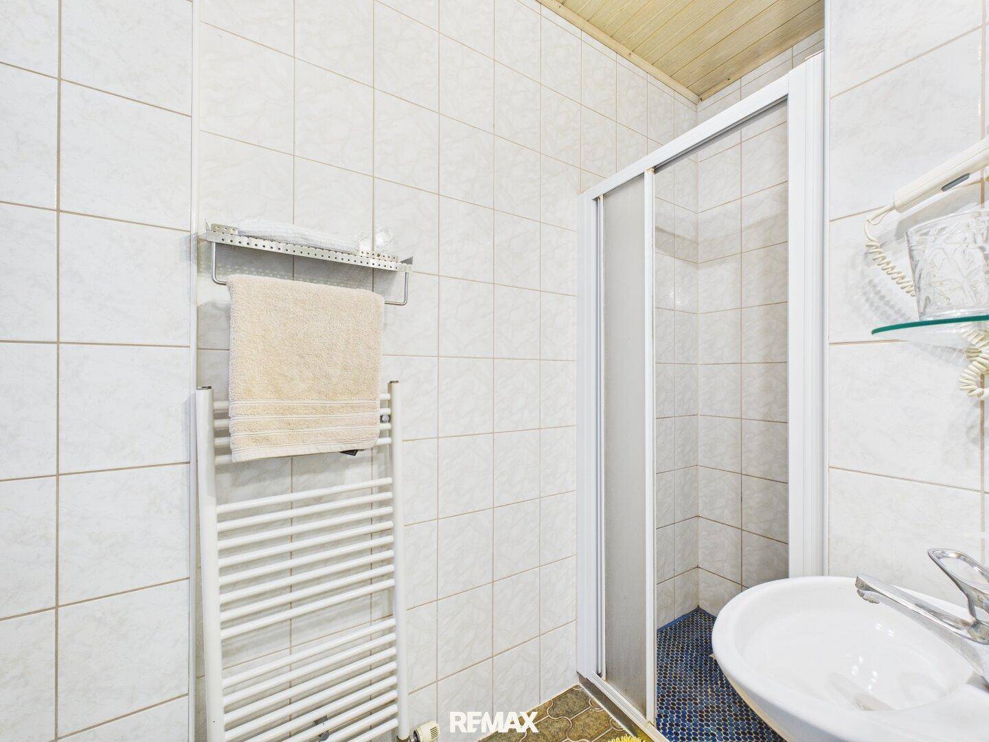 Badezimmer mit Dusche, Waschbecken und beheiztem Handtuchhalter, modern und funktional ausgestattet.