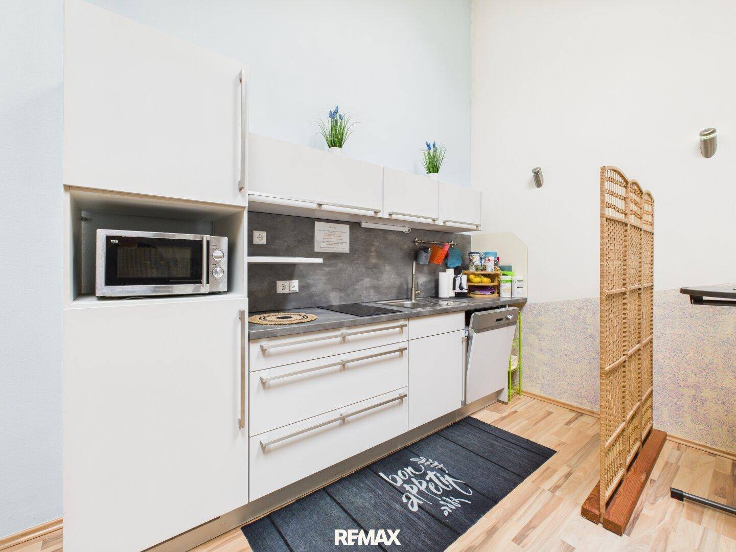 Kleine Küchenzeile mit weißen Schränken, Mikrowelle und Laminatboden, funktional und platzsparend.