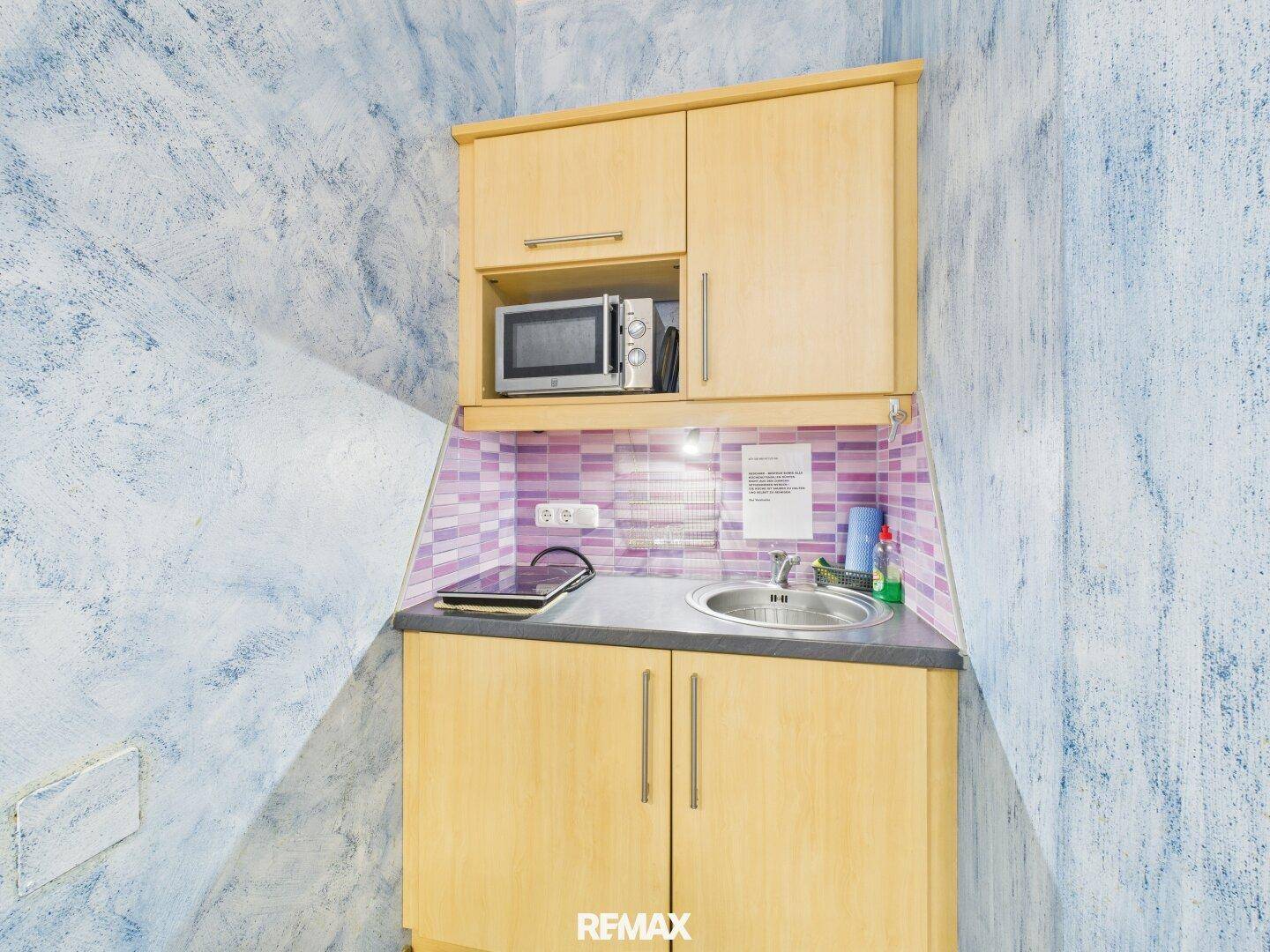 Kleine Küchenzeile mit Holzschränken, Mikrowelle und blauer Wand, funktional und platzsparend.