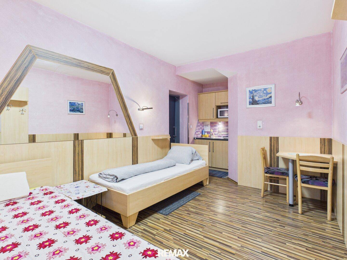 Schlafzimmer mit Einzelbett, kleiner Küchenzeile und rosa Wänden, ideal für Studios.