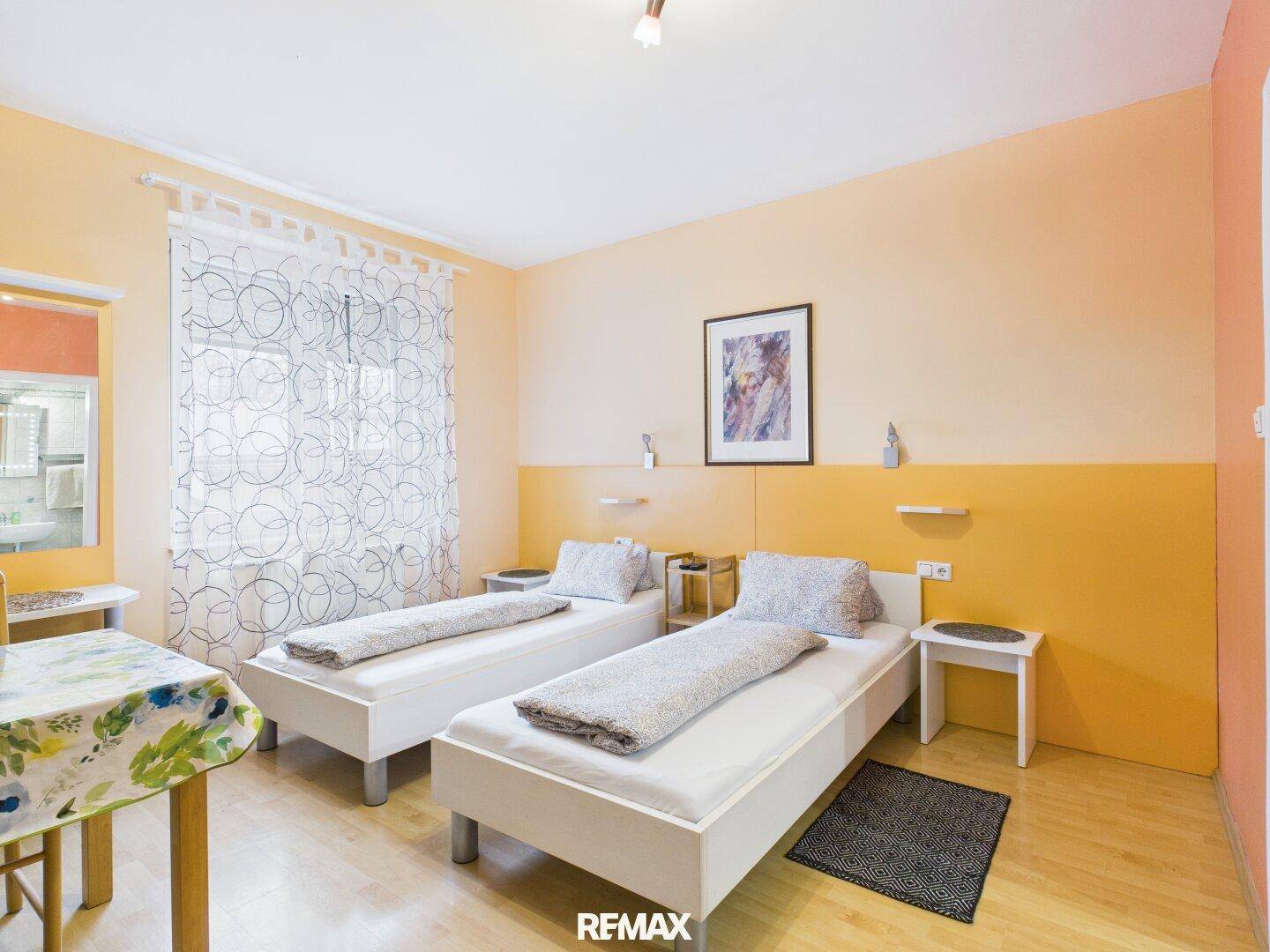 Schlafzimmer mit zwei Einzelbetten, Laminatboden und orangefarbenen Wänden, hell und freundlich.