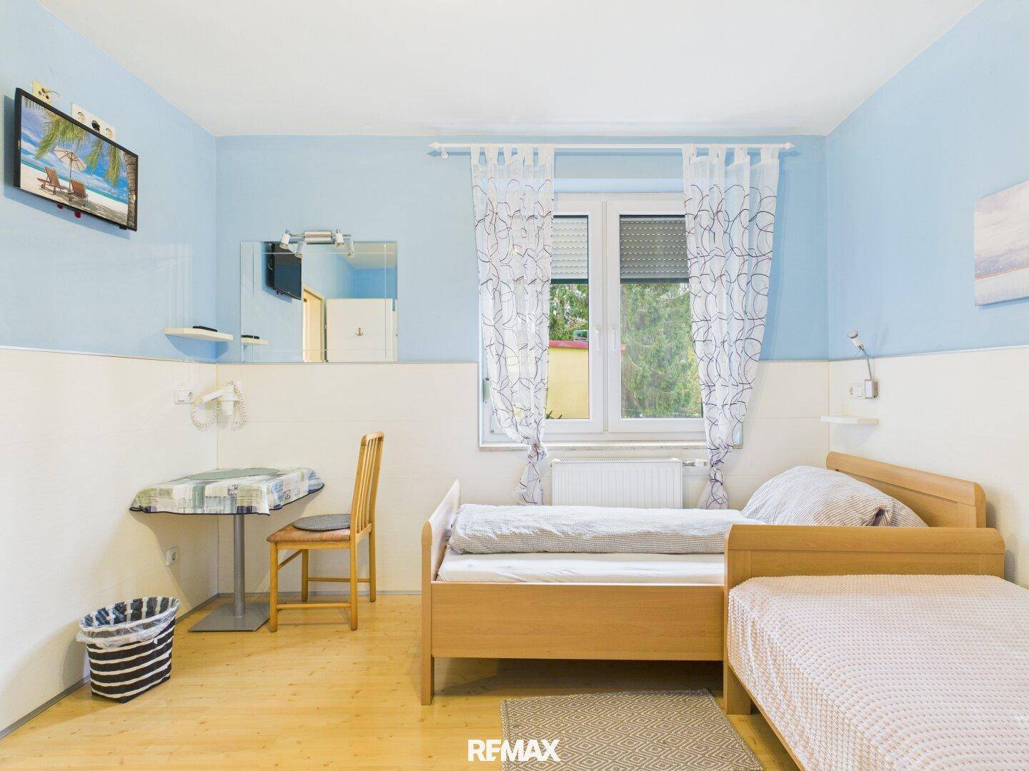 Schlafzimmer mit zwei Betten, Laminatboden und blauen Wänden, bietet eine ruhige Atmosphäre.