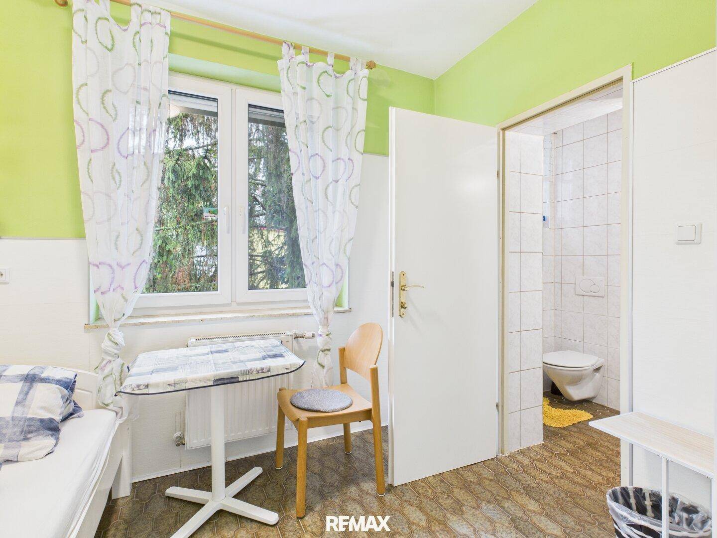 Schlafzimmer mit Einzelbett, Fenster und Zugang zu einem Badezimmer, hell und praktisch.