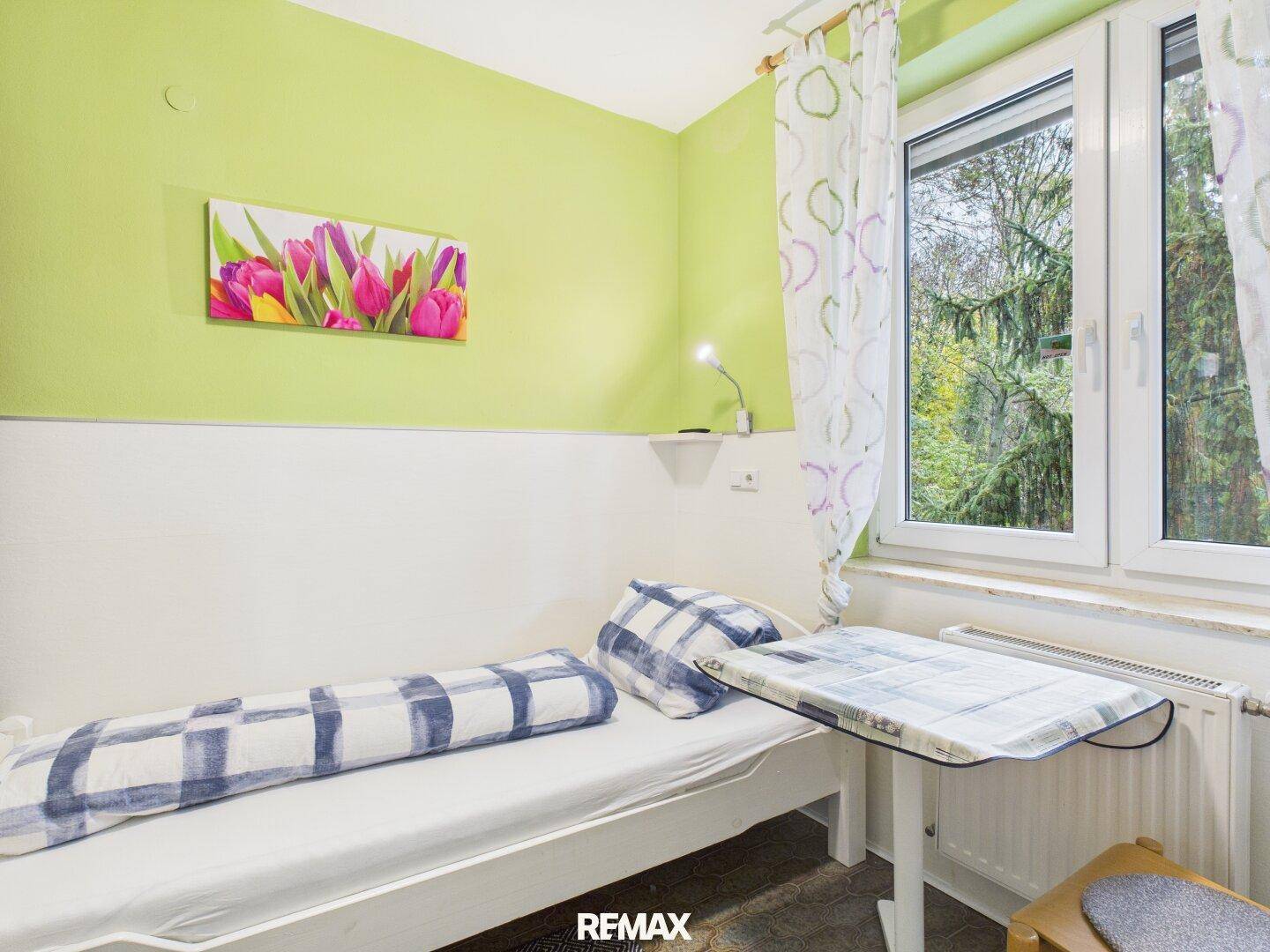 Helles Schlafzimmer mit Einzelbett, grünen Wänden und Fenster, bietet eine angenehme Wohnatmosphäre.
