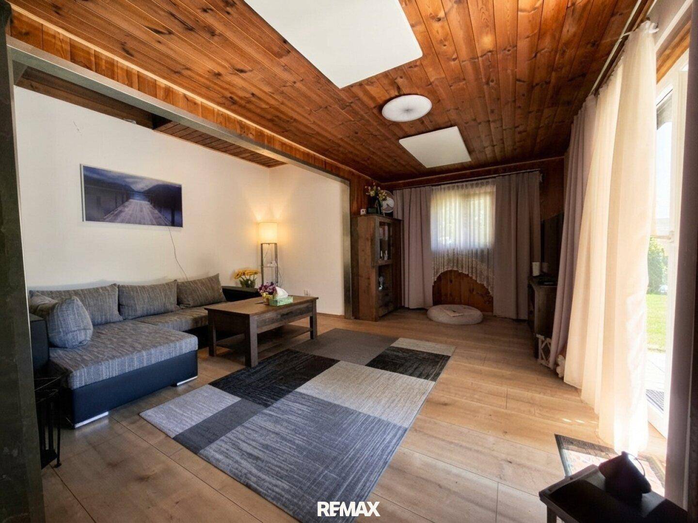 Gemütliches Wohnzimmer mit Holzbalkendecke, Parkettboden und Zugang zur Terrasse.