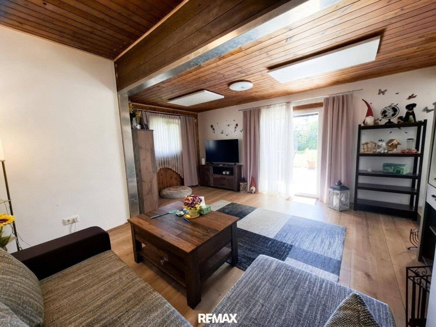 Helles Wohnzimmer mit Holzbalkendecke, bequemer Couch und Blick in den Garten.