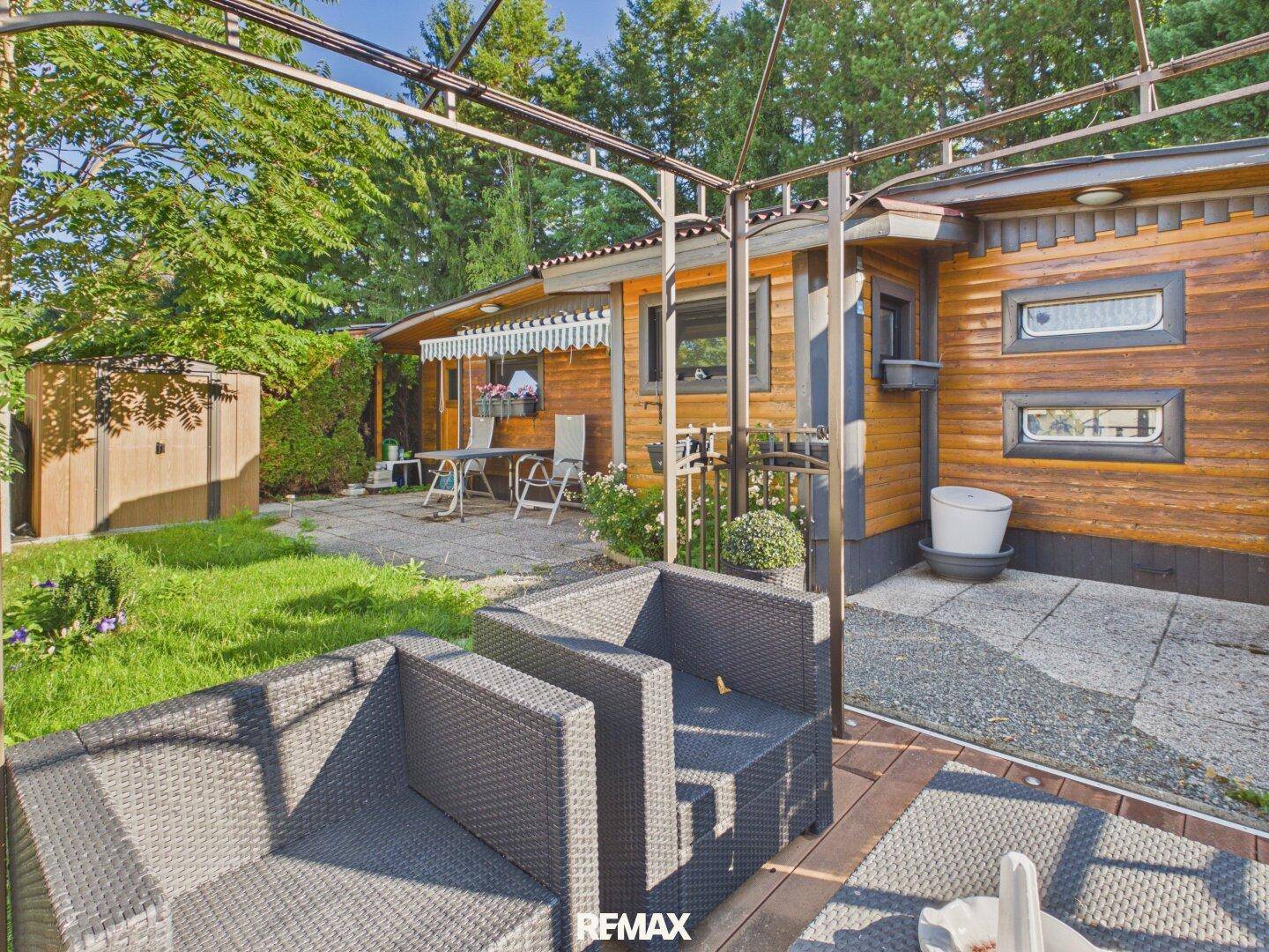 Außenbereich mit Terrasse, Gartenmöbeln und Blick auf das Holzhaus und die grüne Umgebung.