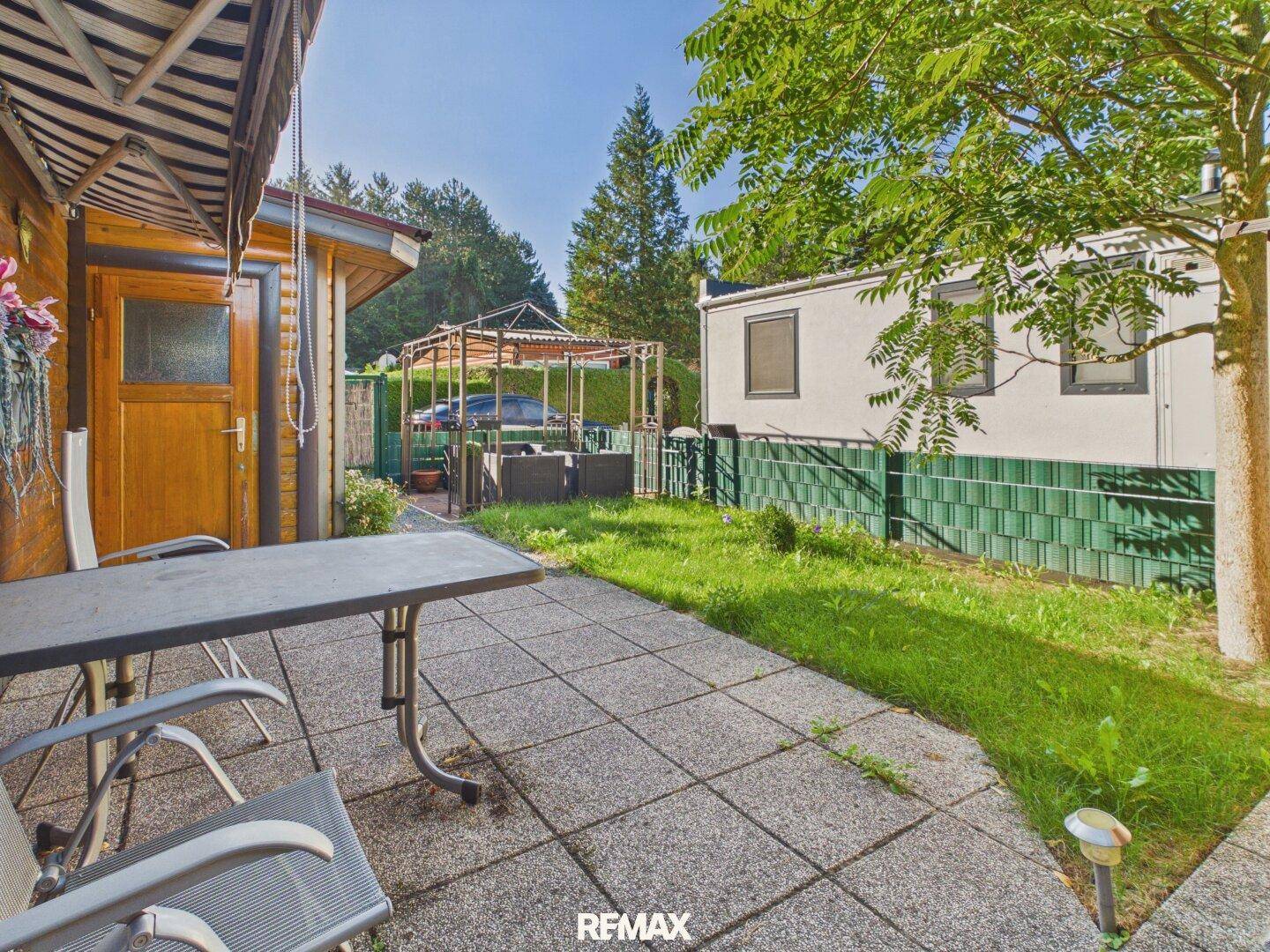 Sonniger Außenbereich mit gepflasterter Terrasse, Rasenfläche und Blick auf die Umgebung.