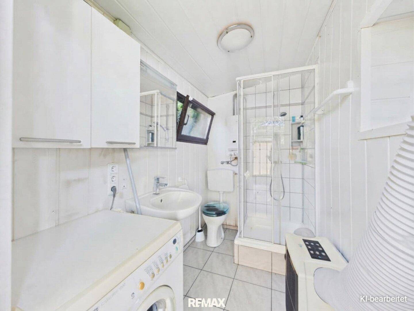 Kleines Badezimmer mit Dusche, Waschbecken, WC und Waschmaschine.