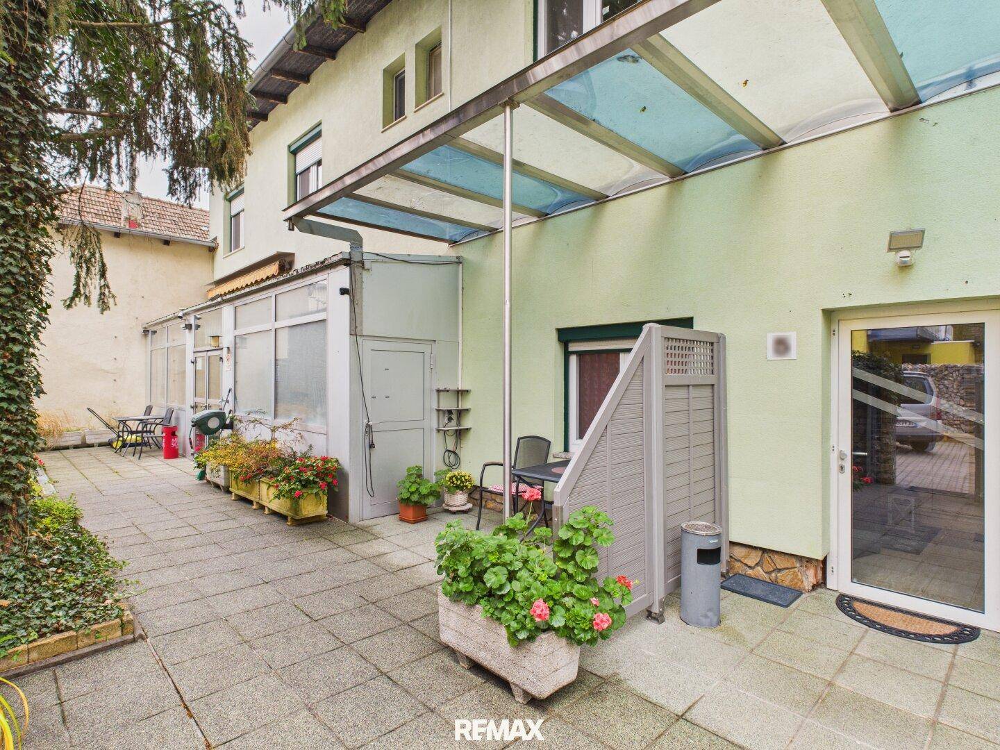Große gepflasterte Terrasse mit Pflanzen und Zugang zum Gebäude, bietet viel Platz im Freien.