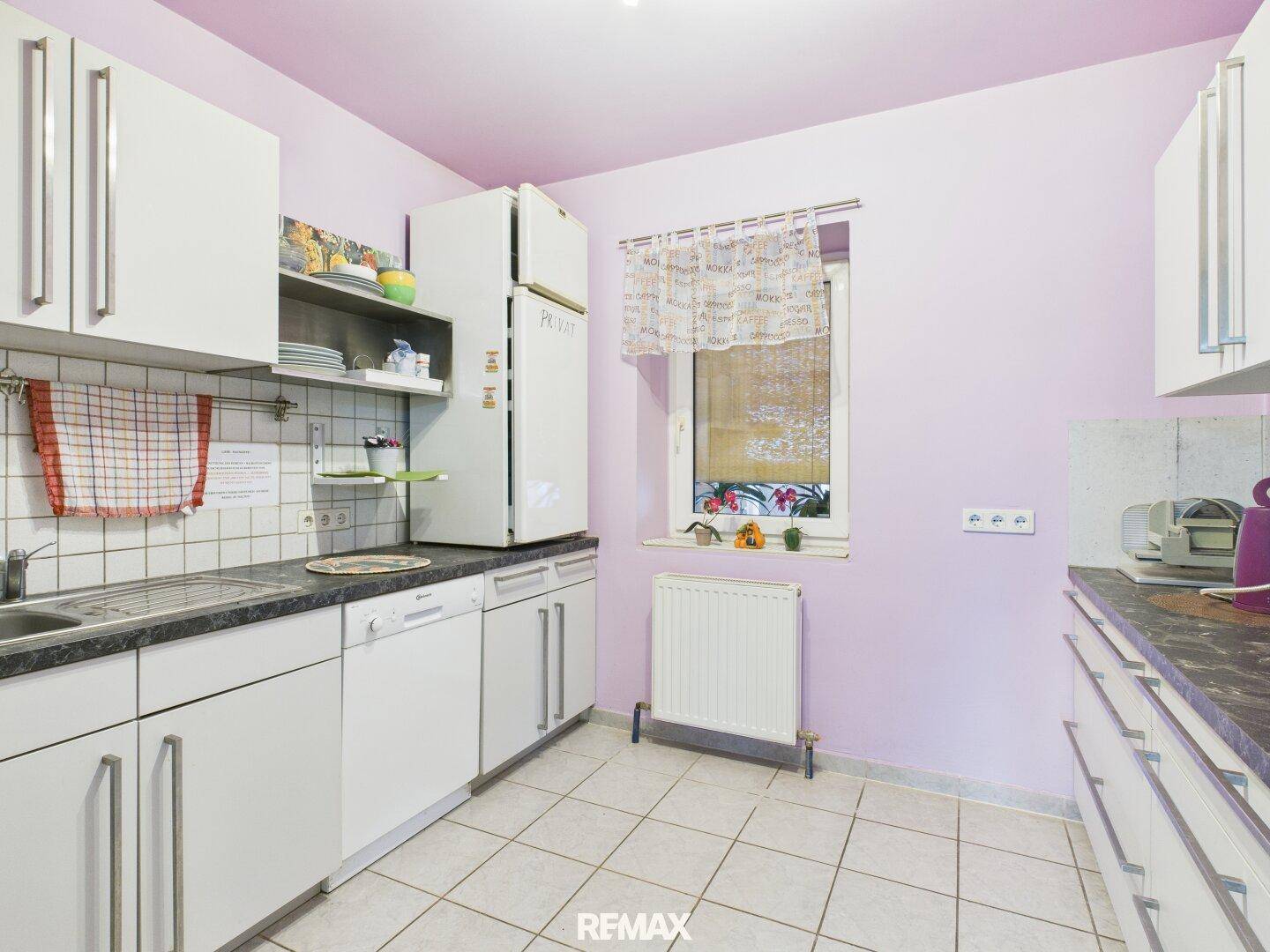 Helle Küche mit weißen Schränken, Fenster und rosa Wänden, ausgestattet mit Geschirrspüler und Kühlschrank.