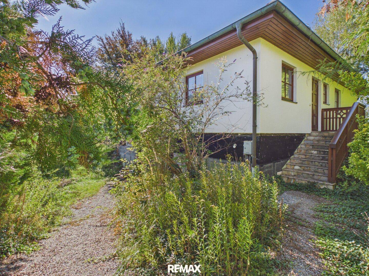 Seitenansicht des Hauses mit Außentreppe und üppiger Vegetation im Gartenbereich.
