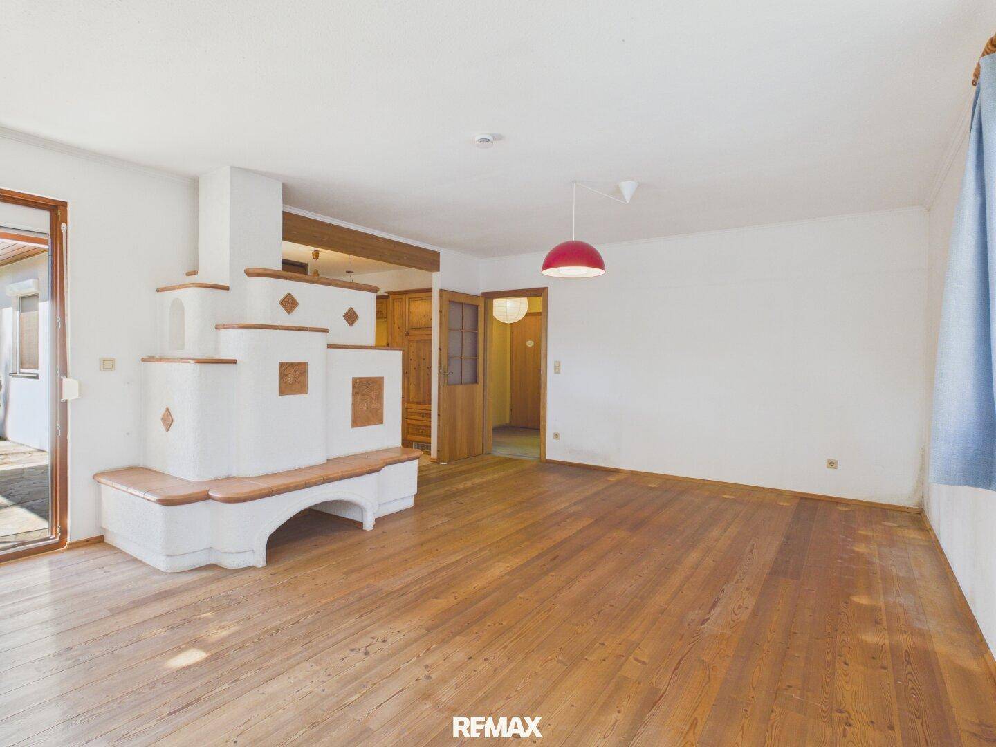 Geräumiges Wohnzimmer mit warmem Holzdielenboden und einem markanten Kachelofen als Mittelpunkt.