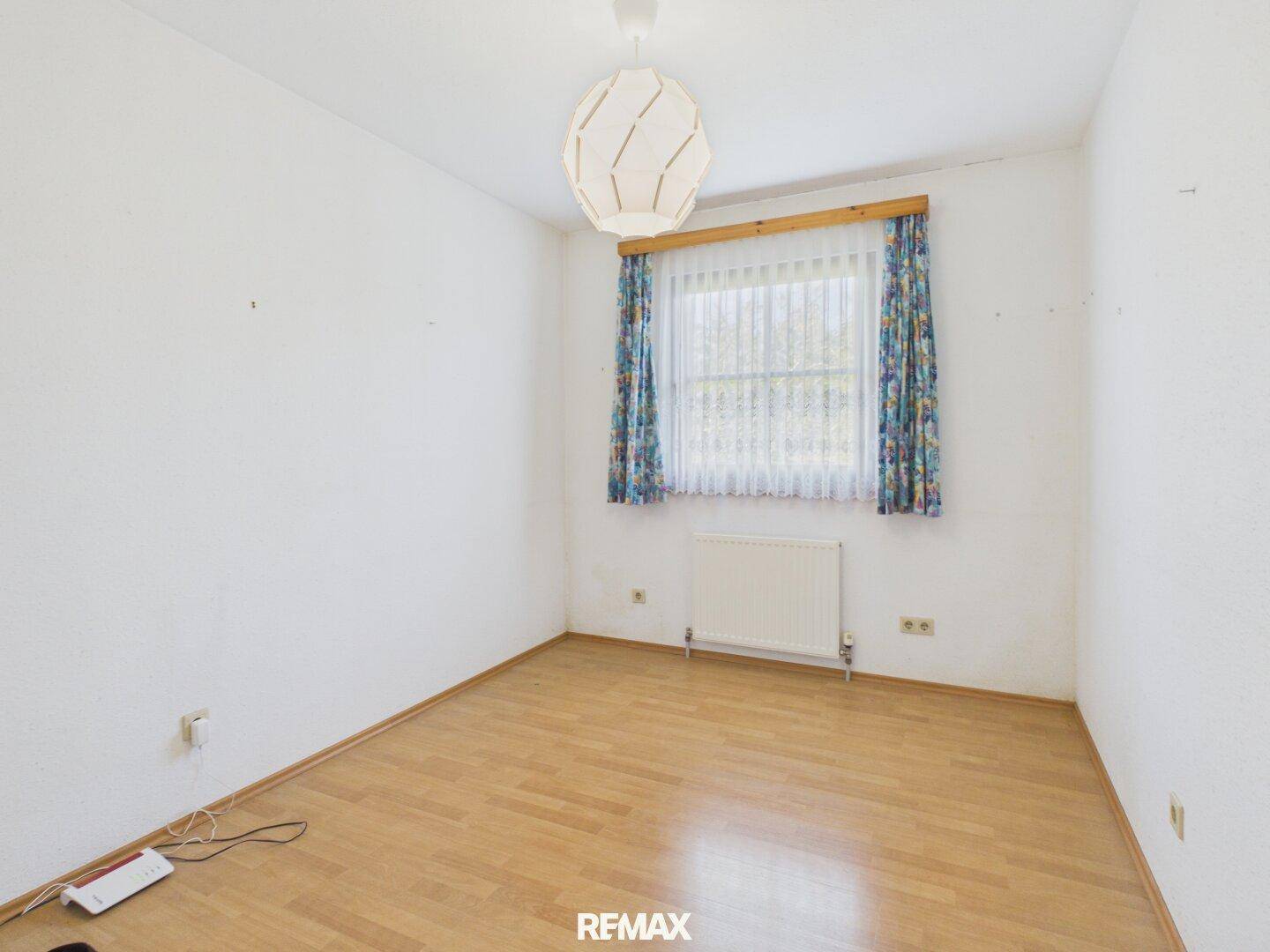 Schlafzimmer mit Laminatboden, weiß gestrichenen Wänden und einem Fenster mit Vorhängen.
