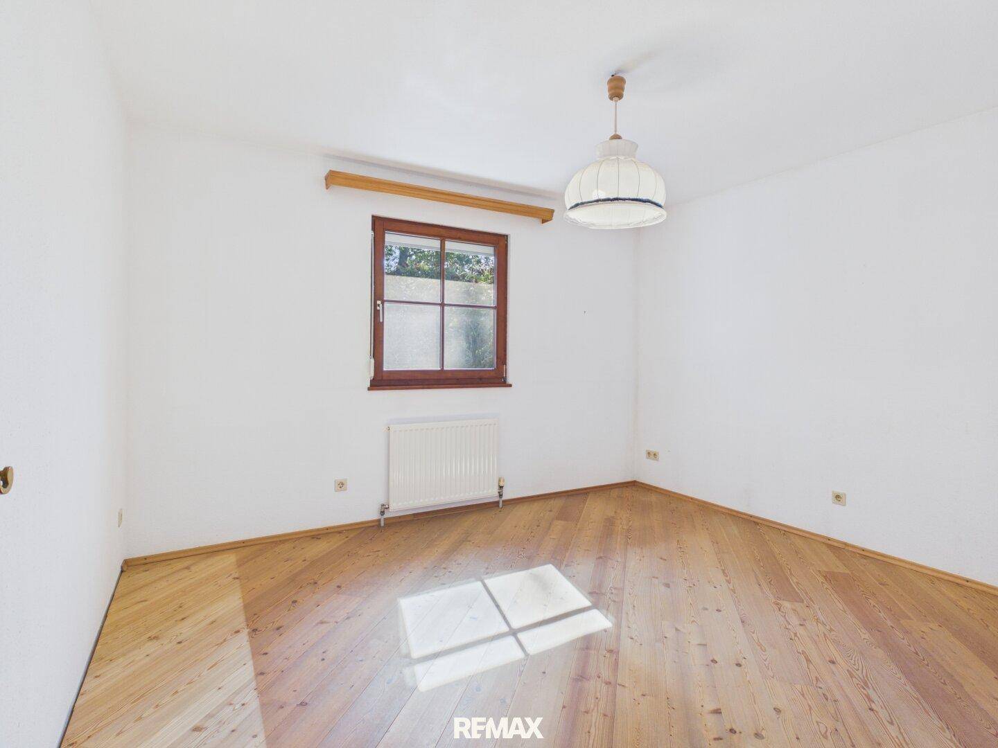 Helles Schlafzimmer mit Holzdielenboden, weiß gestrichenen Wänden und einem Fenster.