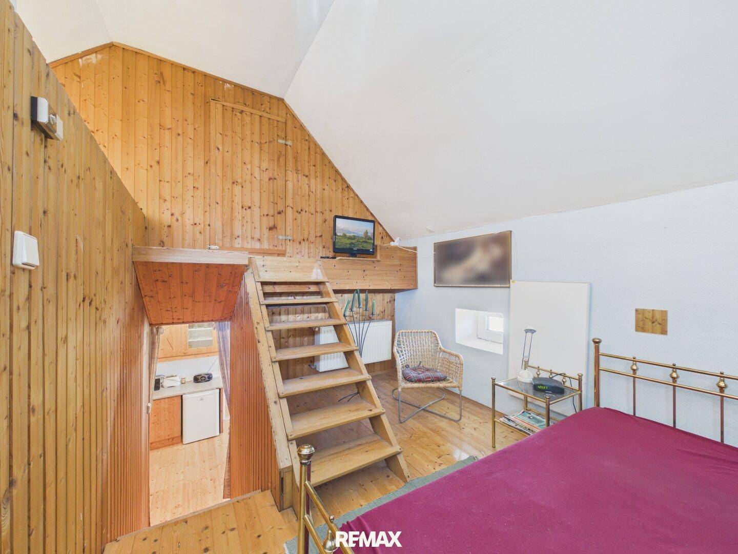Schlafbereich im Dachgeschoss mit Holzvertäfelung, Dachschräge und Treppenzugang.