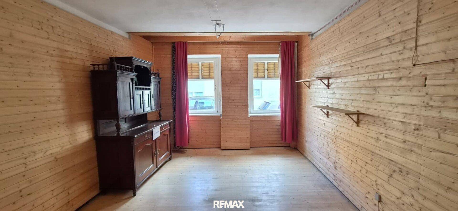 Raum mit Holztäfelung an den Wänden, Holzdielenboden und einem antiken Schrank.
