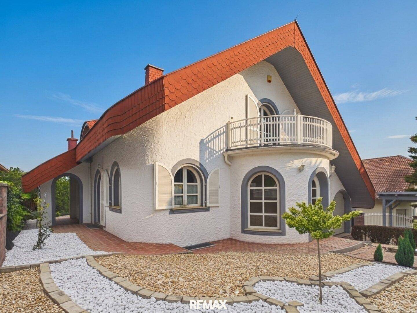 Seitliche Ansicht des Hauses mit weißer Fassade, Rundbogenfenstern und einem kleinen Steingarten.