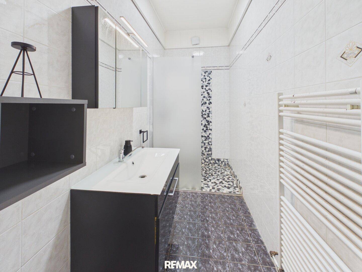 Modernes Badezimmer mit Dusche, dunklen Fliesen und beheiztem Handtuchhalter.