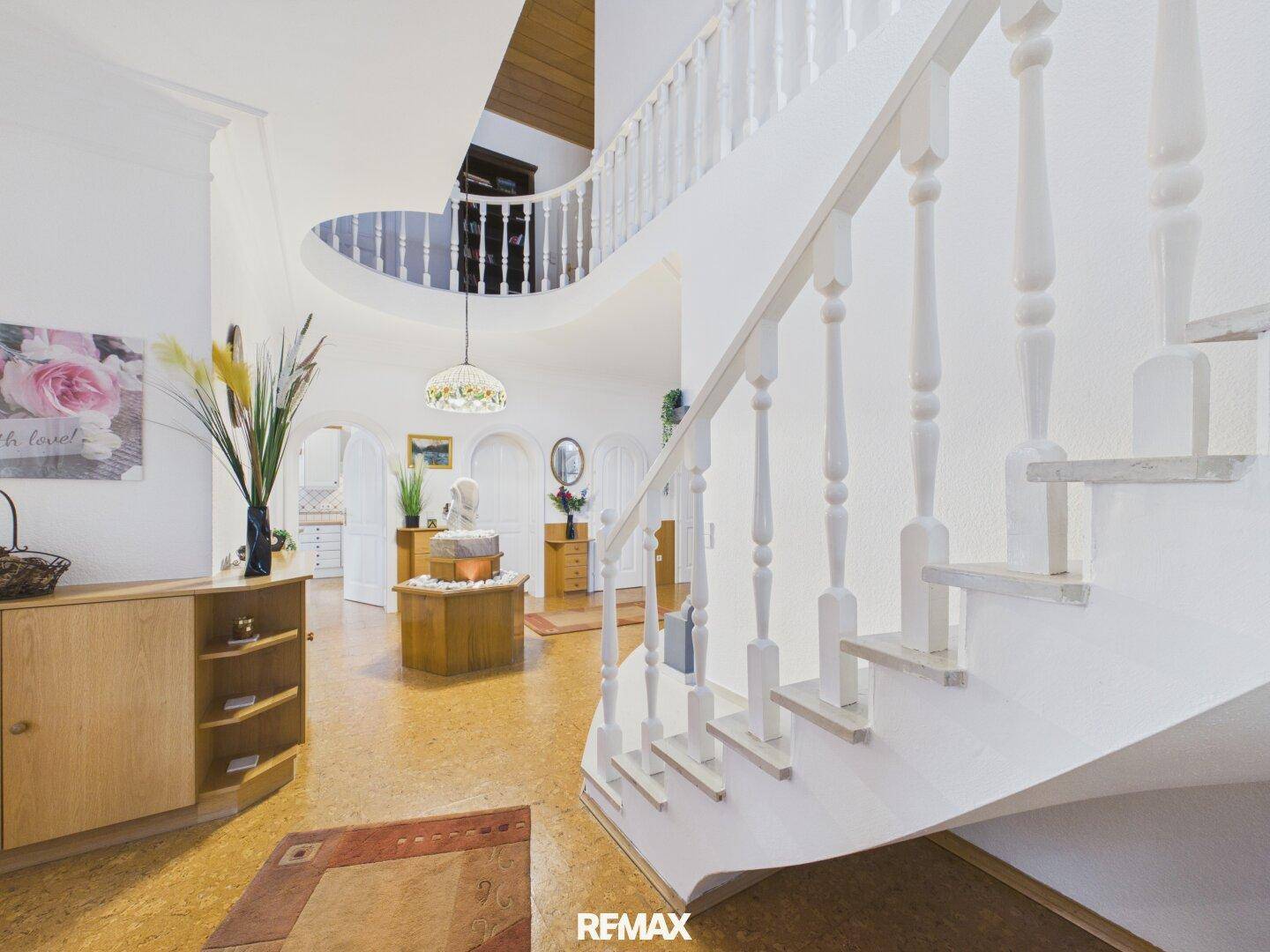 Geräumiger Flur mit geschwungener Treppe, hohen Decken und hellem Ambiente.