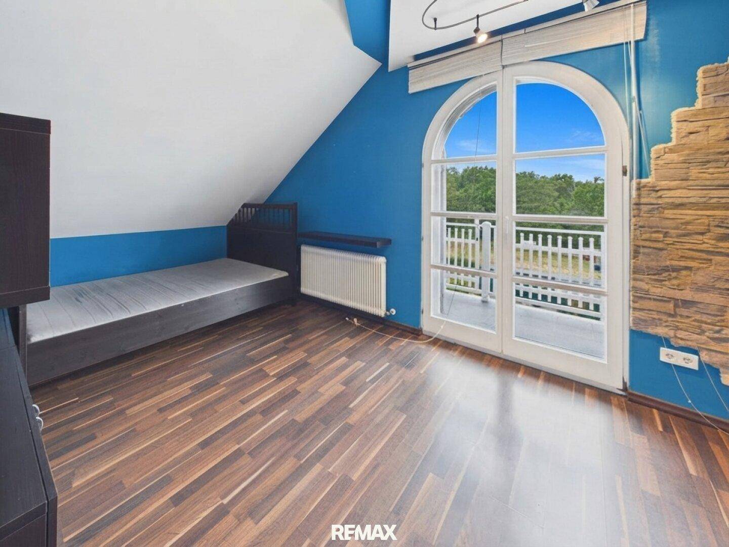 Schlafzimmer mit blauen Wänden, Holzboden und Zugang zu einem französischen Balkon.