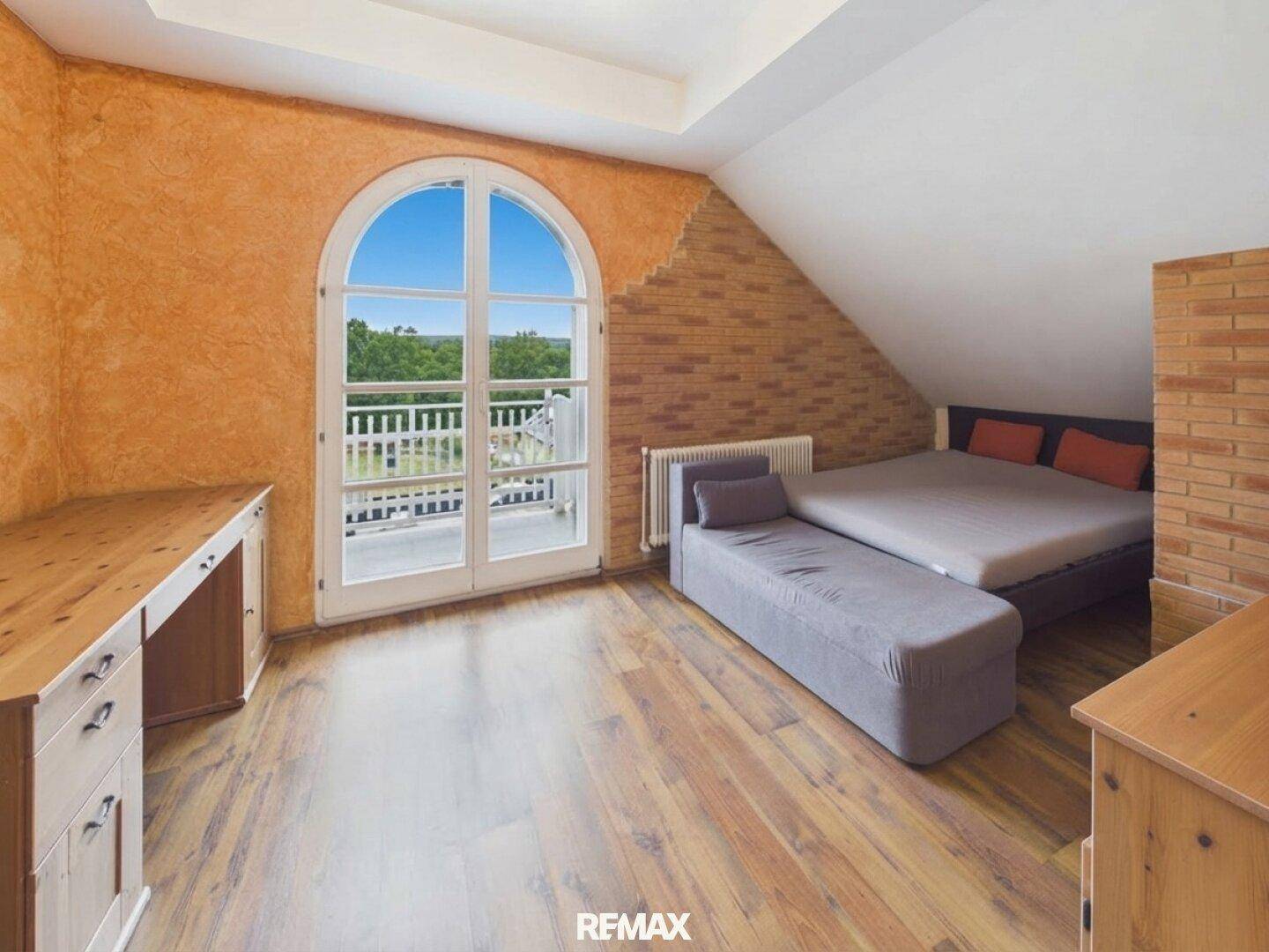 Helles Schlafzimmer mit orangefarbenen Wänden, Holzboden und Zugang zu einem französischen Balkon.