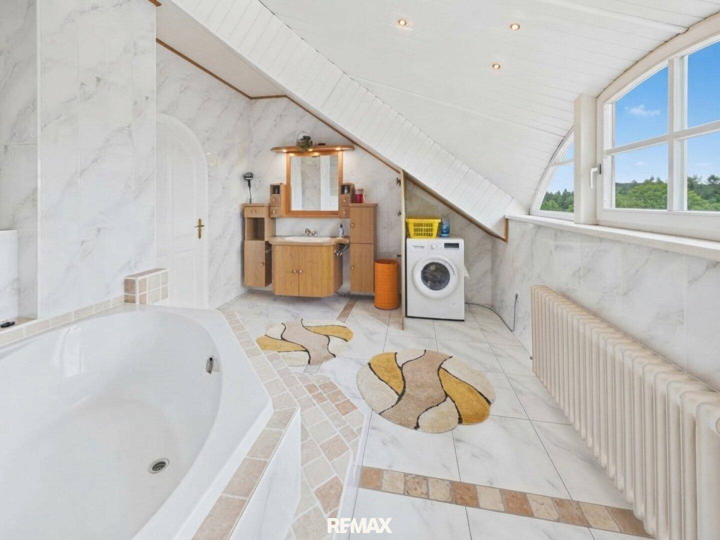 Helles Badezimmer mit Marmorfliesen, Badewanne, Waschmaschine und Dachfenster.